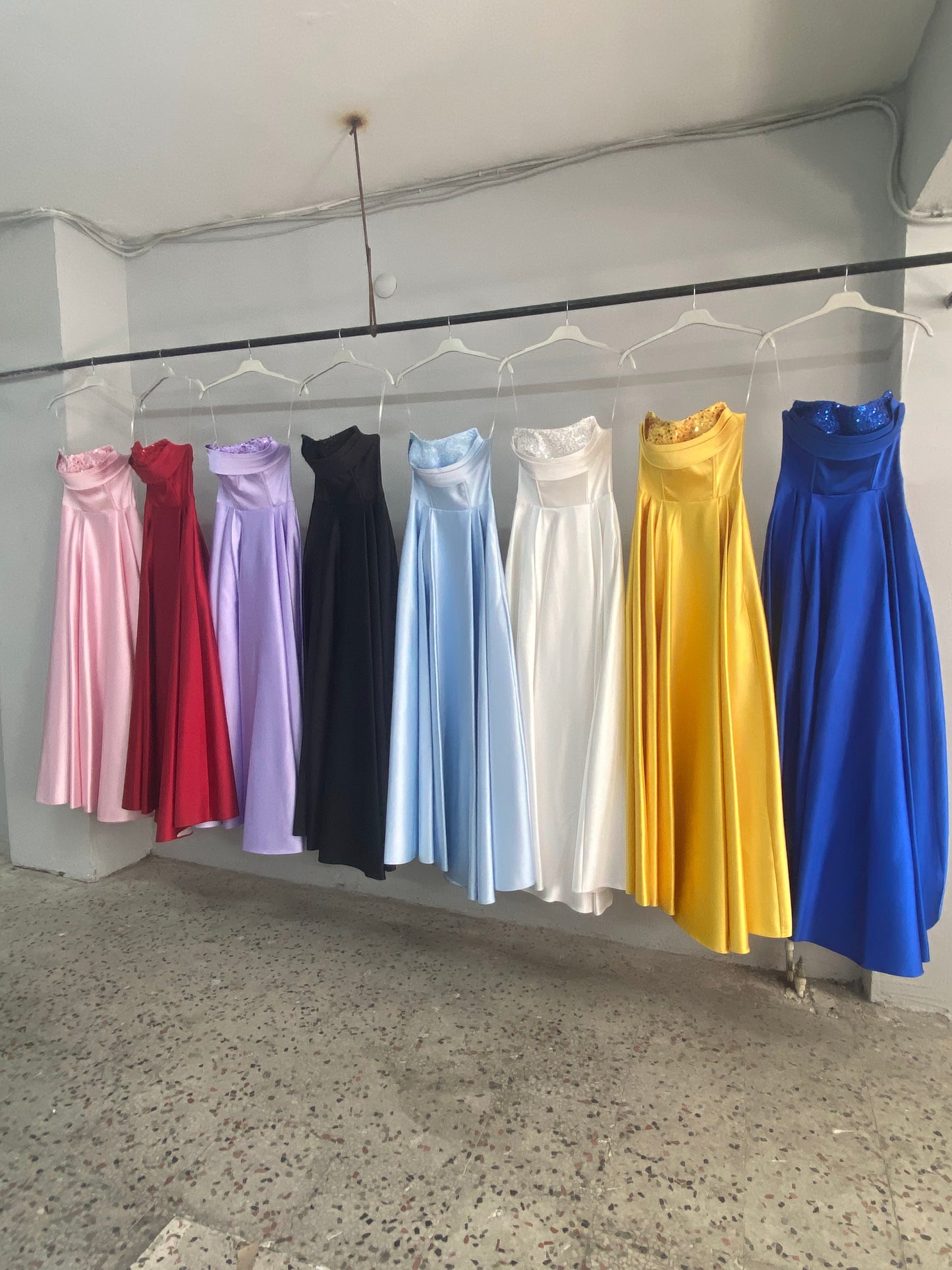 Colorful dresses hanging on a rack against a plain wall.