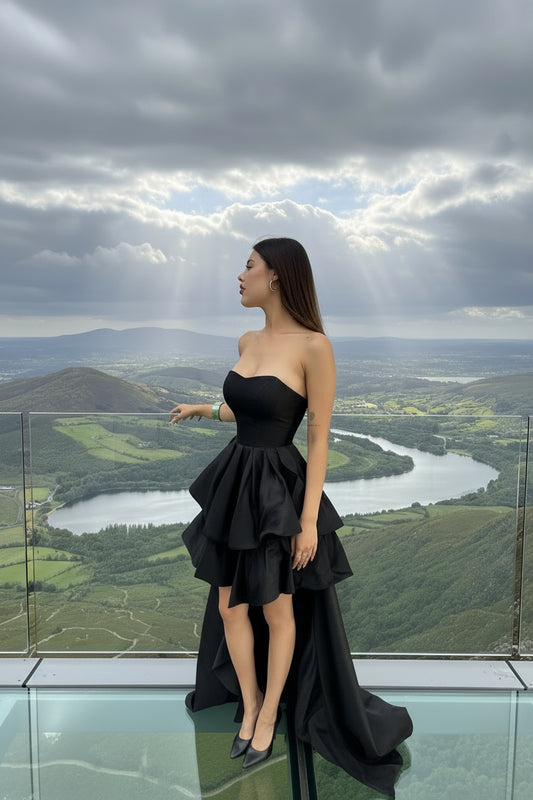 Woman wearing a black strapless dress with a layered skirt against a neutral background