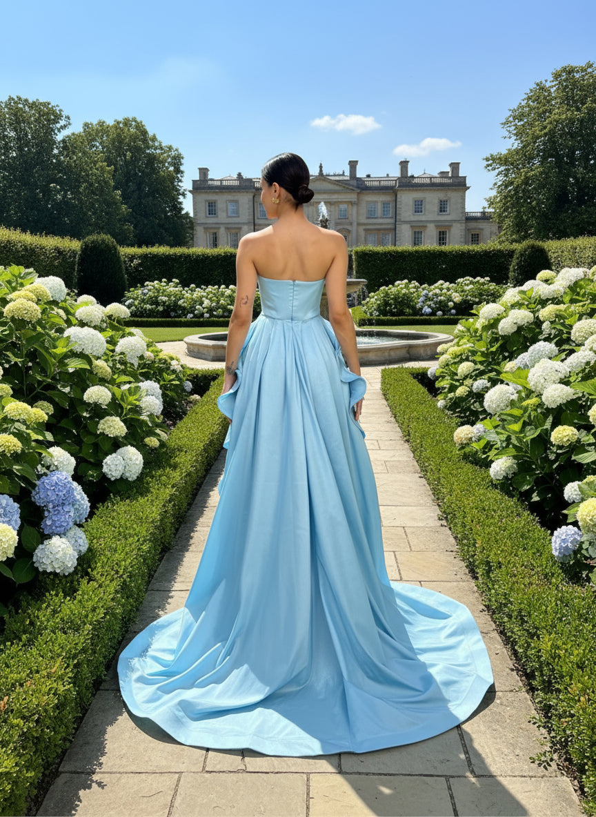 Woman wearing a light blue strapless gown with a long train against a plain background