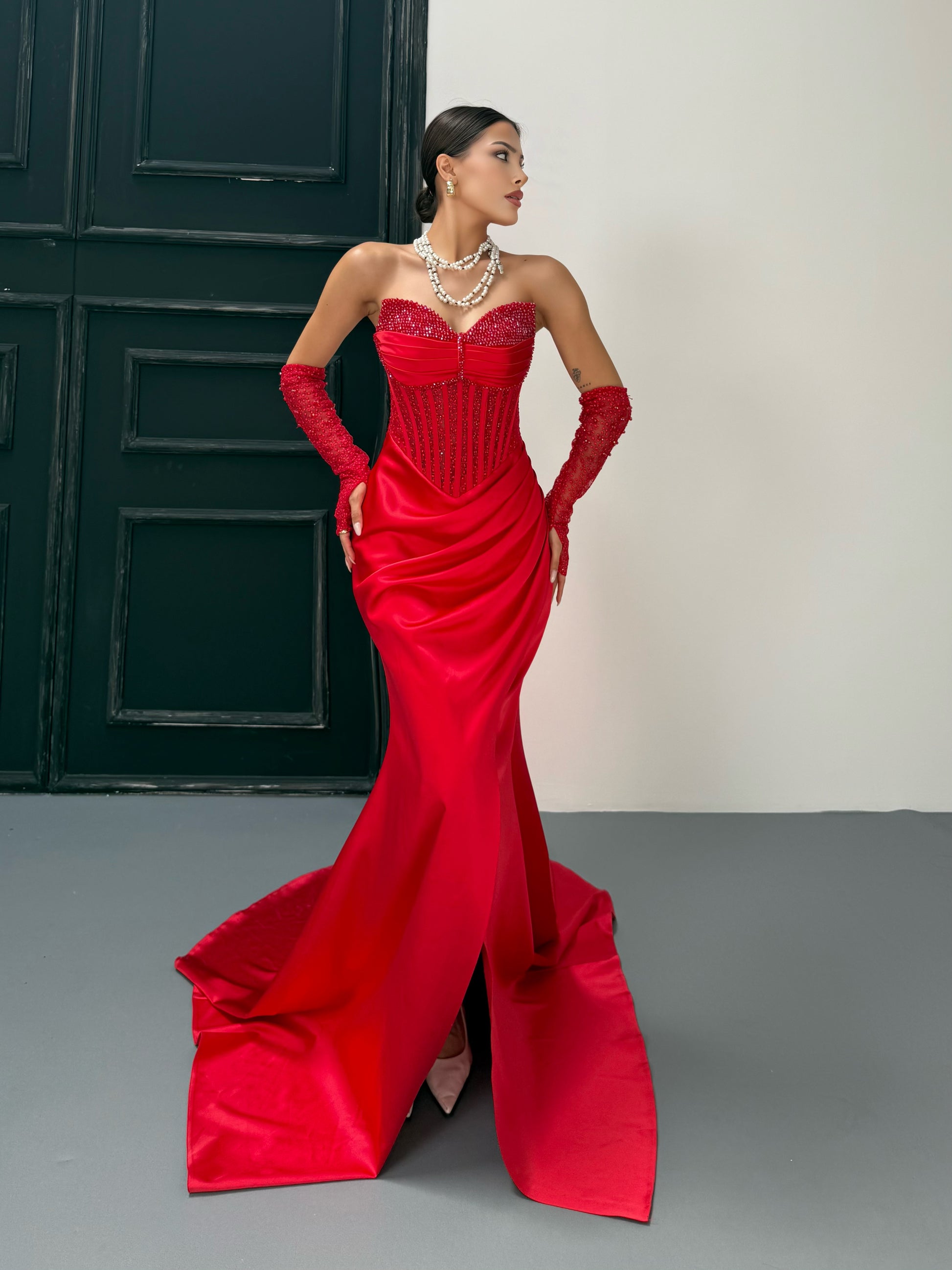 Woman in a red evening gown with gloves standing against a neutral background