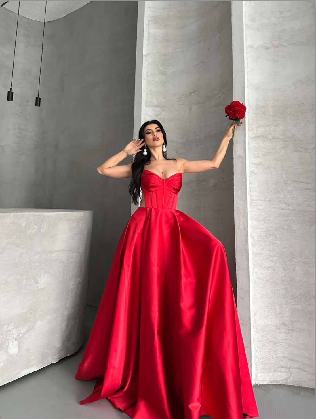 Woman in a red dress holding a red rose against a gray wall.